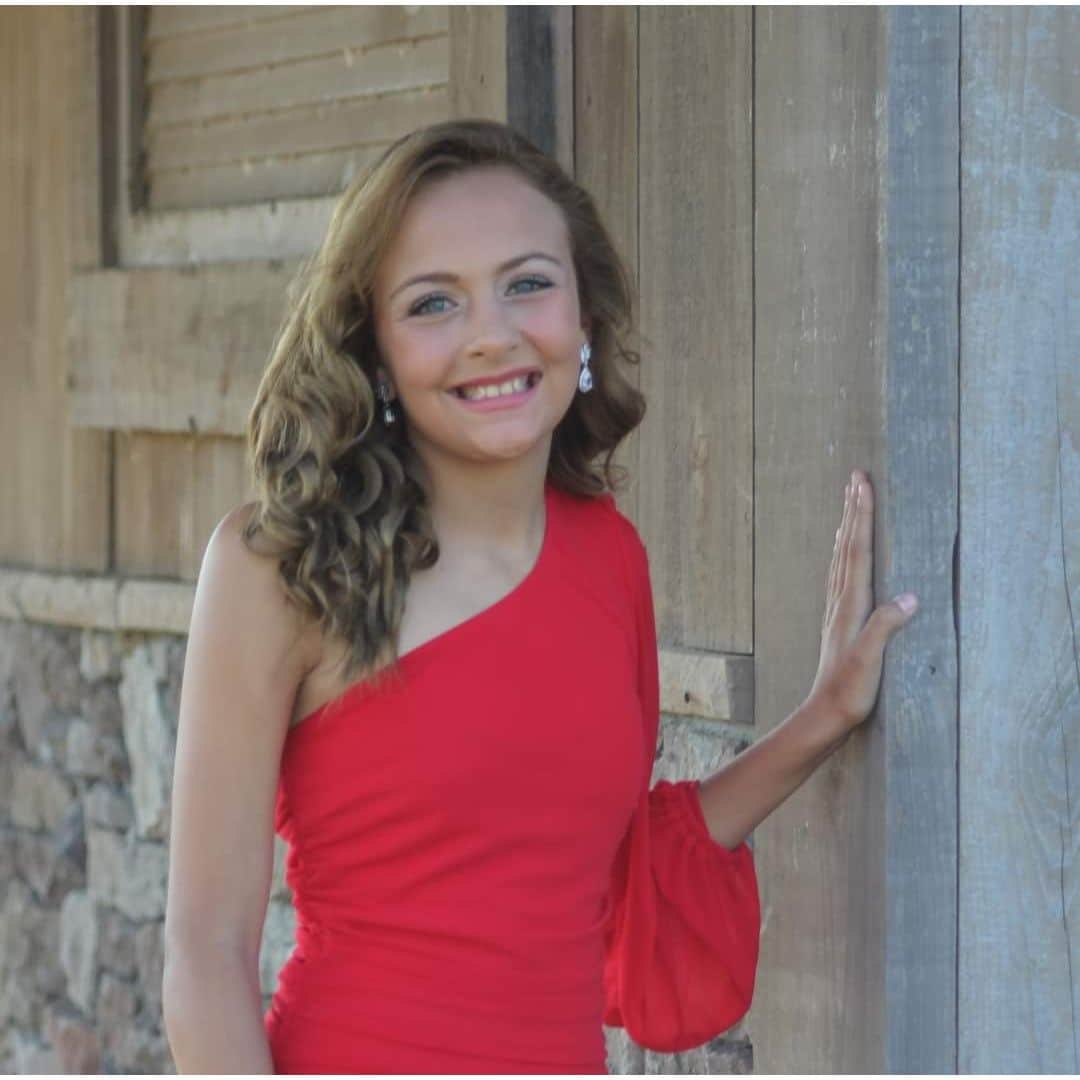 Smiling girl in red dress by rustic wall.