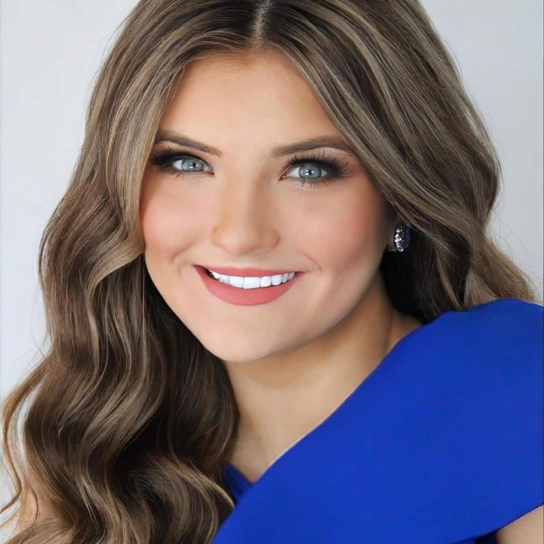 Smiling woman with wavy hair in blue dress.