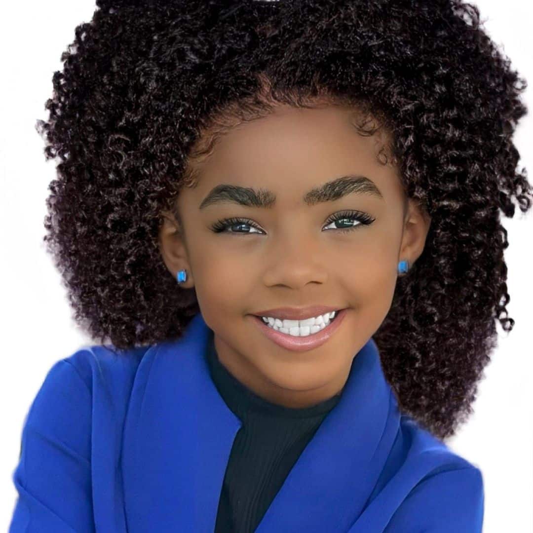 Smiling child with curly hair and blue outfit.