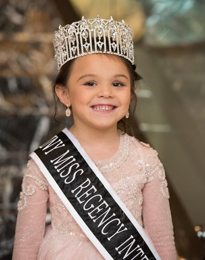 Young girl with crown and sash smiling.